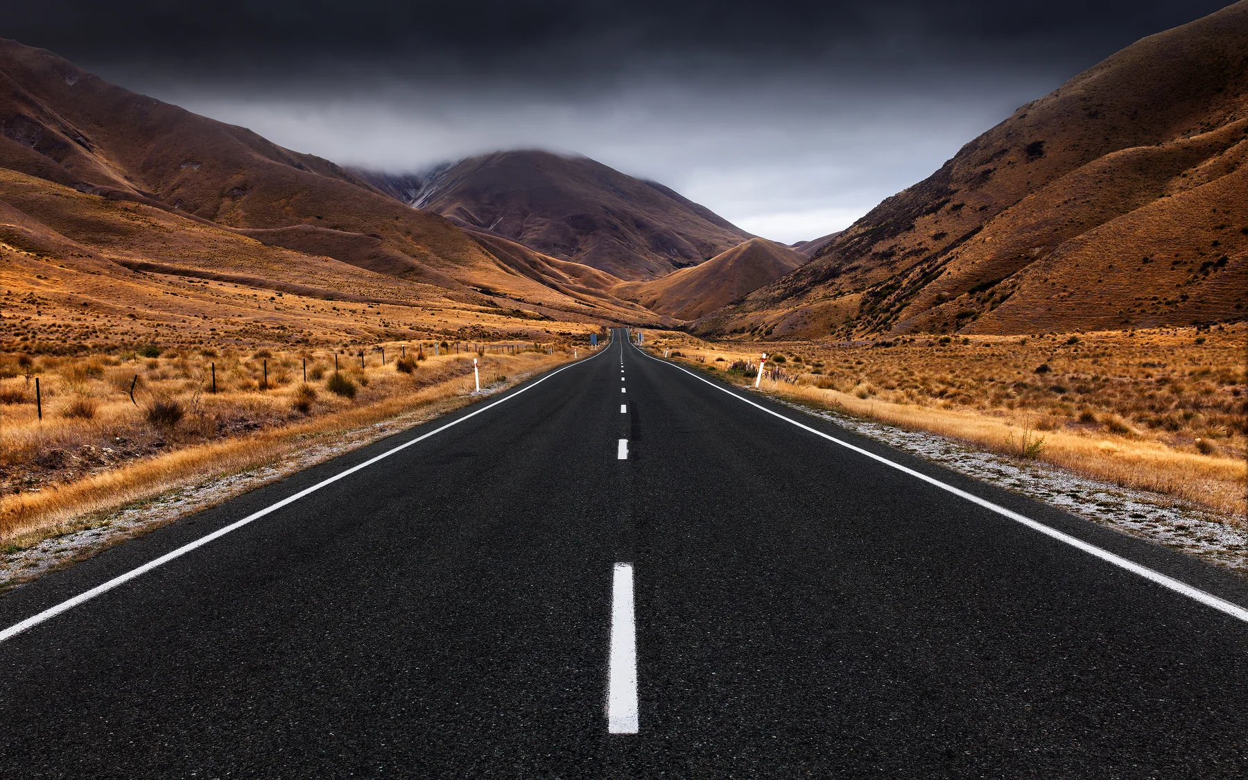 A high-definition Lindis Pass road running through warm golden tussock hills