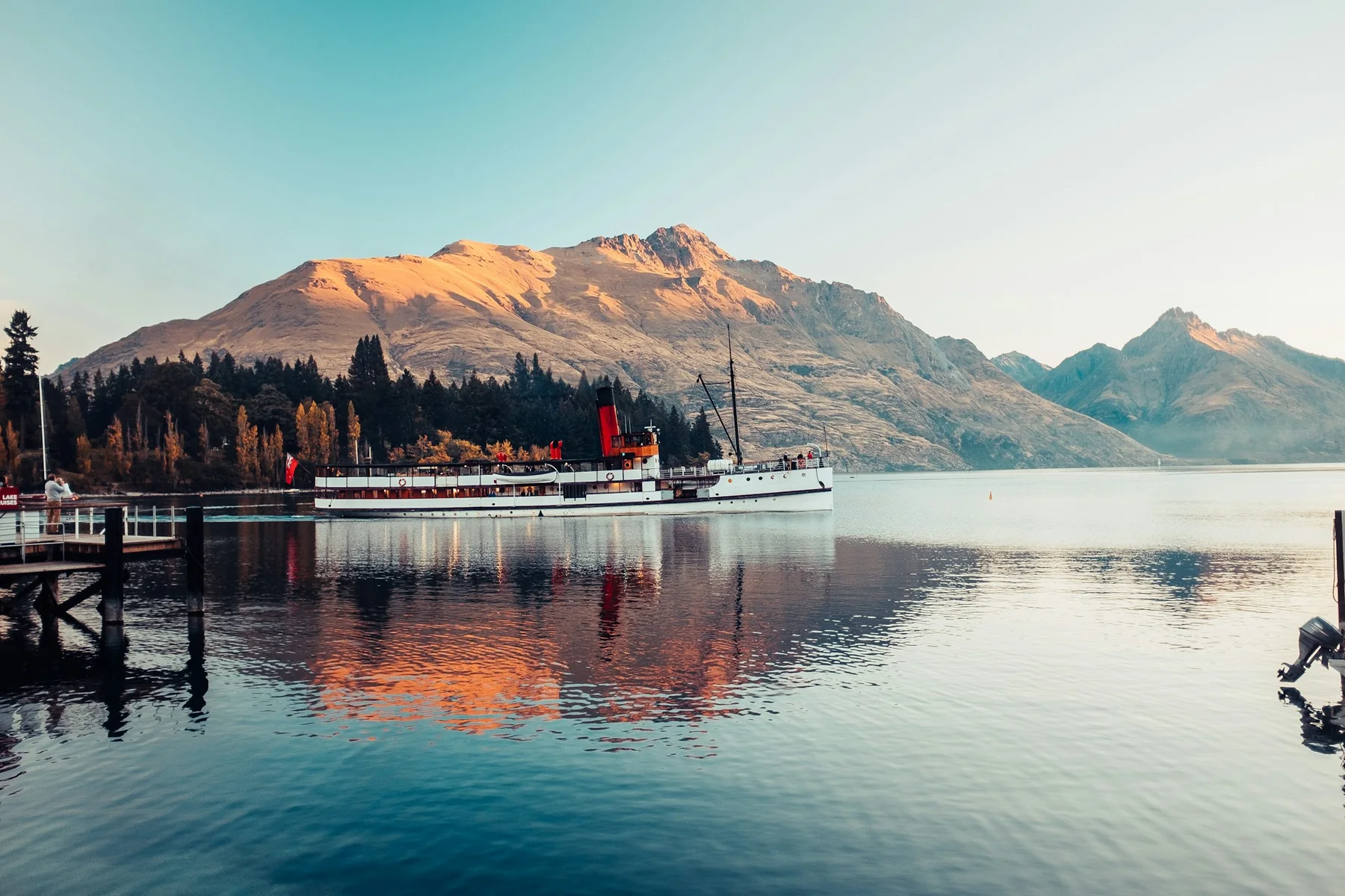 Lake Wakatipu shoreline with boats, trees, and mountains beyond