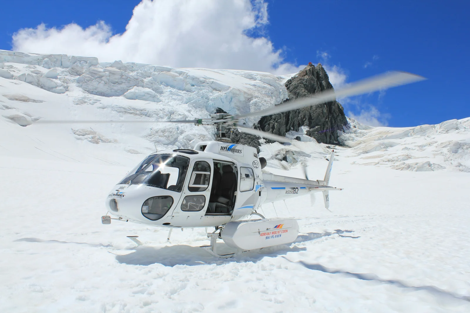 Helicopter on snow beneath alpine ice and blue sky